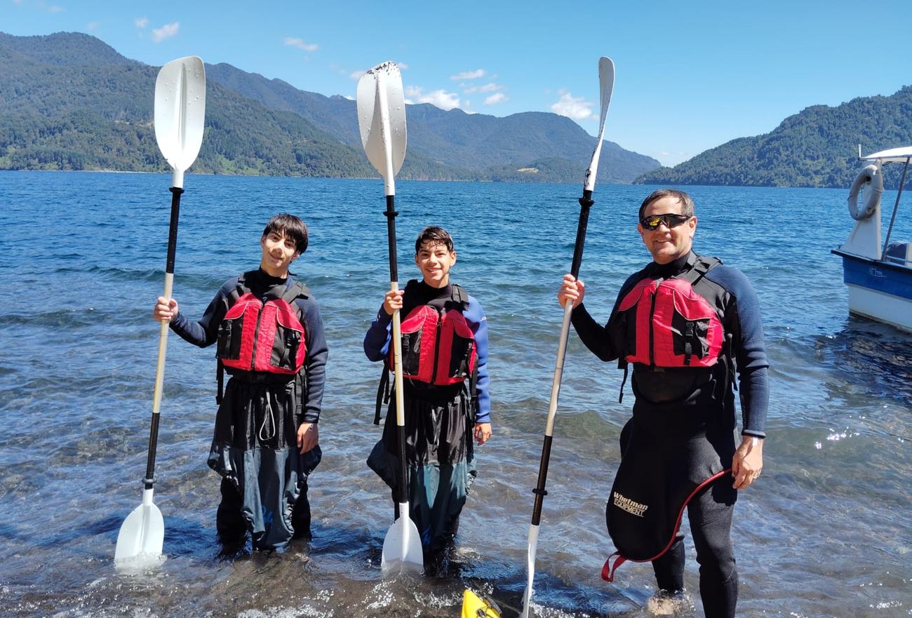 Dos adolescentes y su instructor con remos y chalecos a orillas del lago